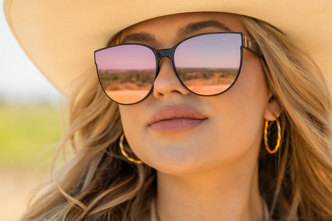 Cowgirl wearing the Heat Wave Visual Womens Carat Sunglasses with black frame and rose gold lenses.