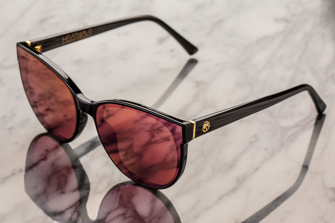 Sitting on a marble table is the Heat Wave Visual Womens Carat Sunglasses with black frame and rose gold lenses.