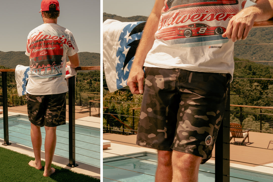 Man standing in from of his pool wearing the Heat Wave Visual Midnight Camo Board Shorts. 