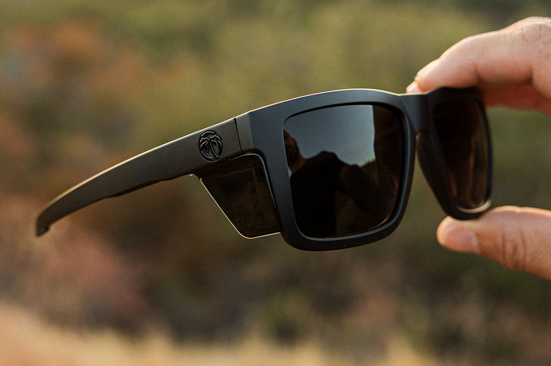 Hand holding the Heat Wave Visual Performance XL Vise Sunglasses with black frame and ultra black lenses.