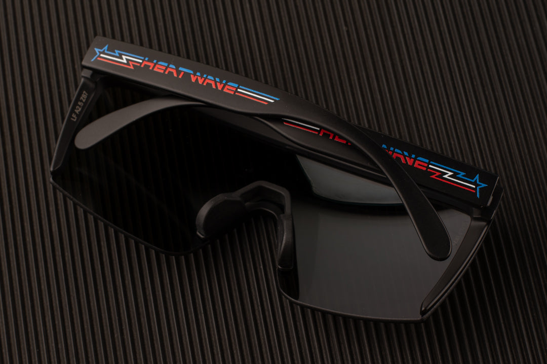 Laying on a table is the Heat Wave Visual Lazer Face Sunglasses with black frame, speed star arms and galaxy blue lens. 