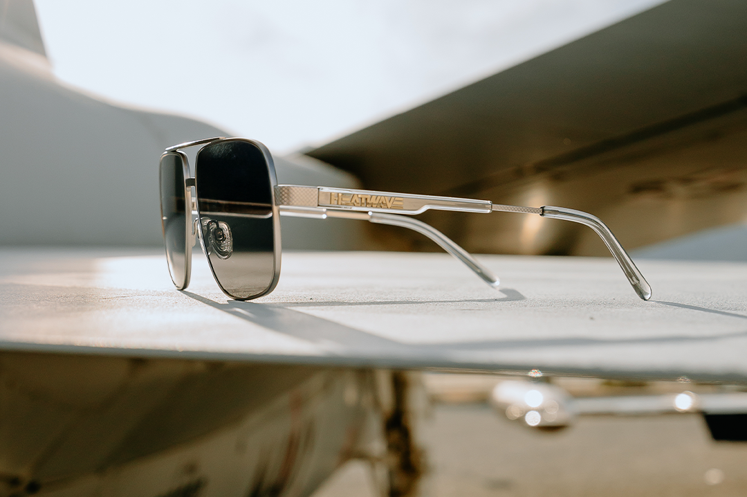 The Heat Wave Visual Nimitz Sunglasses with gun metal frame and black lenses sitting on the wings of a plane.